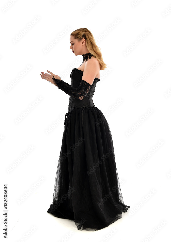 full length portrait of a blonde girl wearing black gothic gown. standing pose, isolated on white background.