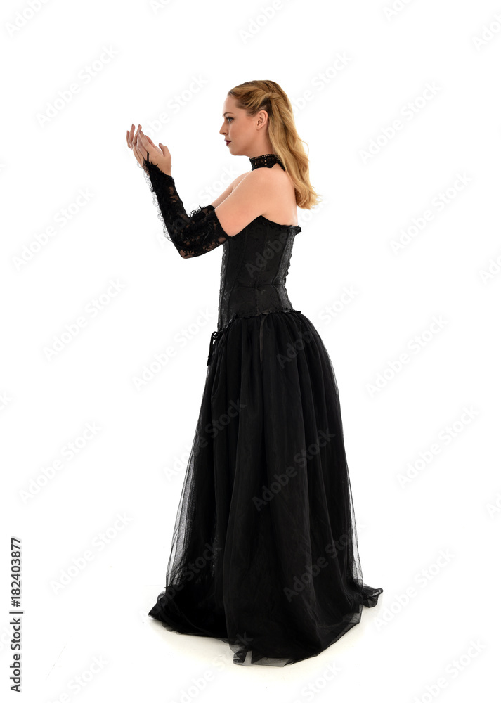 full length portrait of a blonde girl wearing black gothic gown. standing pose, isolated on white background.