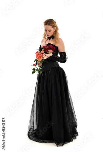full length portrait of a blonde girl wearing black gothic gown. standing pose  isolated on white background.