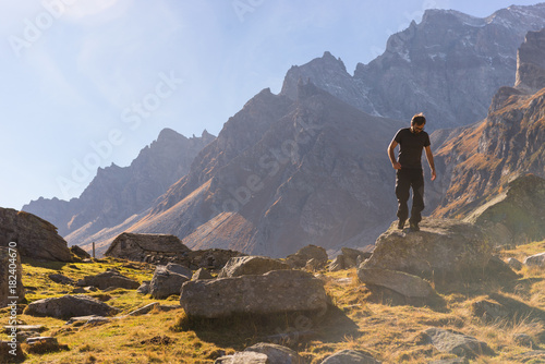 Young adult man hiker climb down a rock on mountain in sunny autumn day on Alps in Italy outdoor.