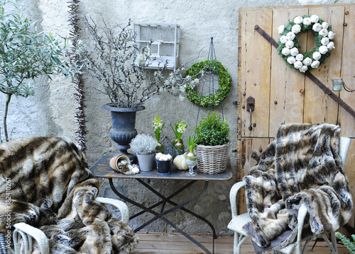 Terrasse et son atmosphère hivernale avec chaises en osier, plaid en fausses fourrures, buis, et branches séchées