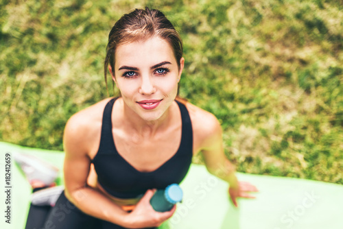 Cute sporty girl relaxing outdoor after training with bottle of water