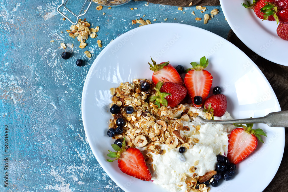 Good morning! Breakfast with yoghurt, granola and strawberries on a blue, concrete background.