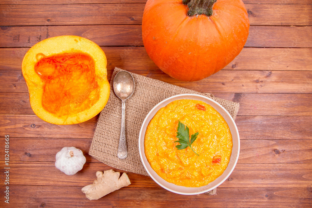 Pumpkin soup and pumpkin, ginger and garlic on a wooden background