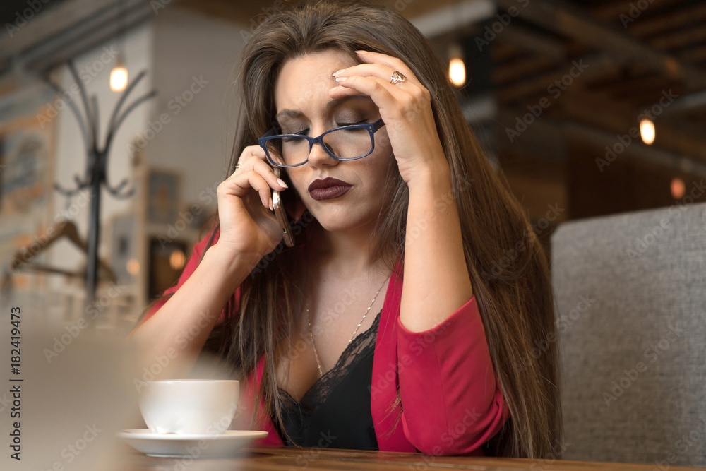 sad young woman talking on the phone in a cafe during her coffee break. Beautiful woman working by the window in the cafe sad young woman talking on the phone in a cafe during her coffee break. Beautiful woman working by the window in the cafe