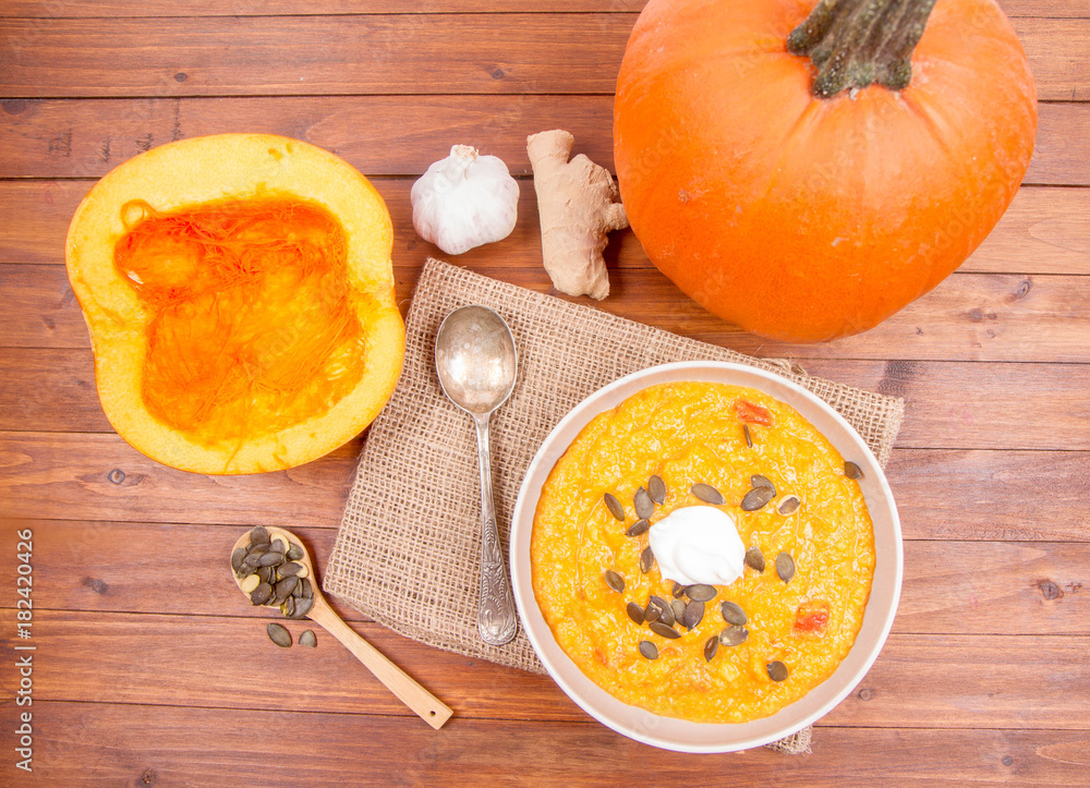 Pumpkin soup and pumpkins, pumpkin seeds, ginger and garlic on a wooden background