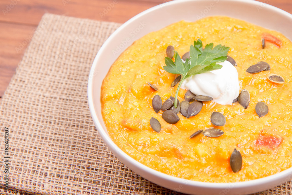 Pumpkin and carrot soup decorated with cream, parsley and pumpkin seeds on a wooden background Pumpkin and carrot soup decorated with cream, parsley and pumpkin seeds on a wooden background