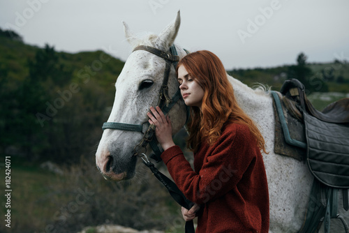 Beautiful young woman walking with a white horse in the mountains