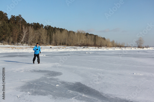 Man in a blue jacket running across the ice of a frozen river, Ob Reservoir, Russia
