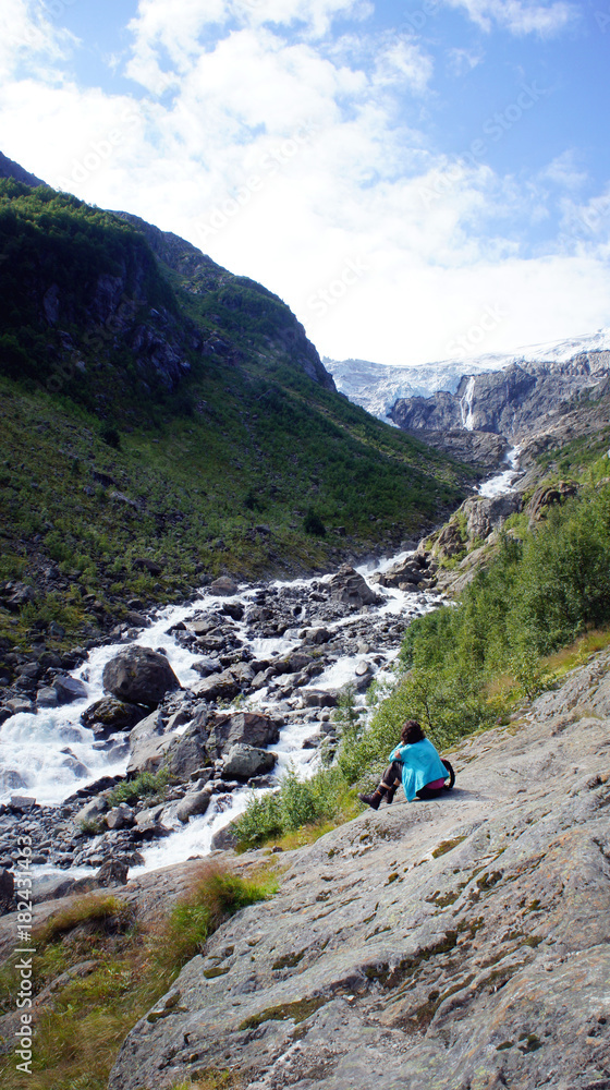 Scenic view of Buerdalen valley and fast river, tourist is sitting and looking at beautiful nature (Folgefonna National Park) in Odda, Hordaland, Norway