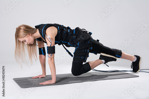 Blonde in an electric muscular suit for stimulation makes an exercise on the rug. photo