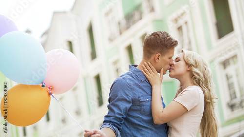 Tablou pe pânză Sweet couple kissing in street, romantic date with colorful balloons, happiness