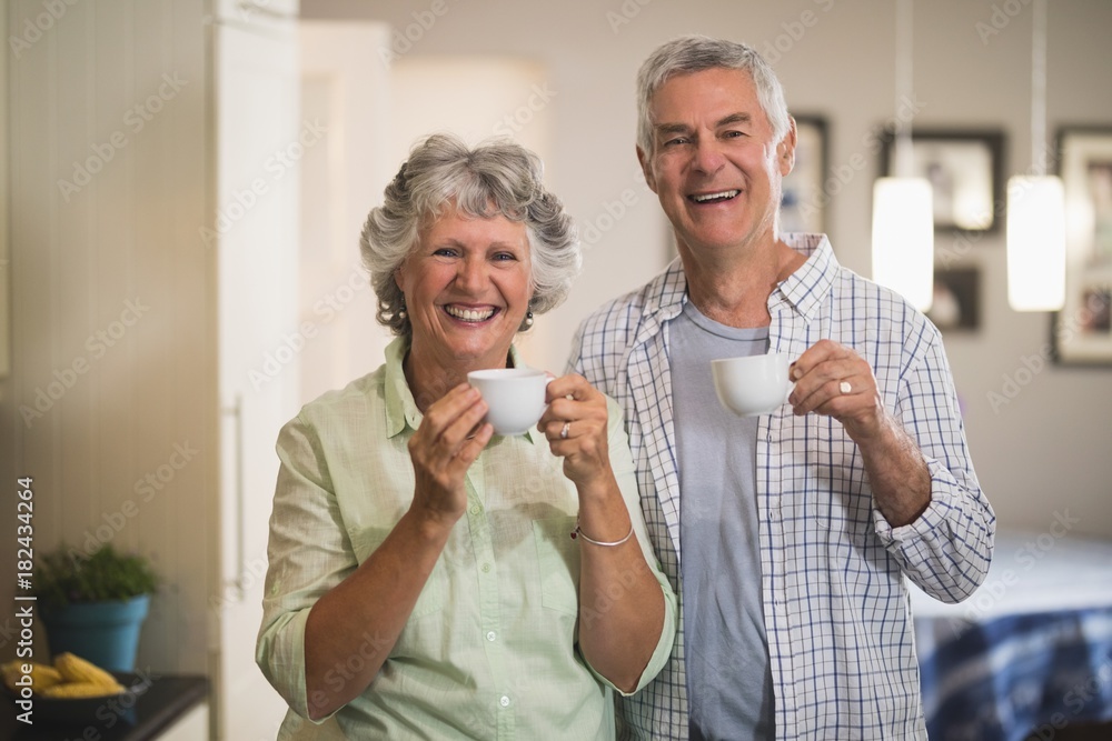 Portrait of happy senior couple holding cups in kitchen Portrait of happy senior couple holding cups in kitchen