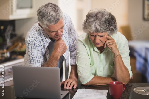 Serious senior cpouple reading documents by laptop on table