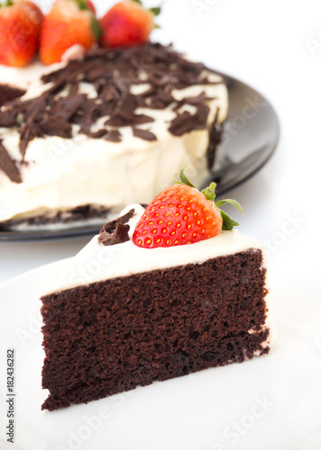Chocolate cake decorate with whipping cream, sliced chocolate and fresh strawberries. On white plate over white background. Sweet dessert for celebrate.