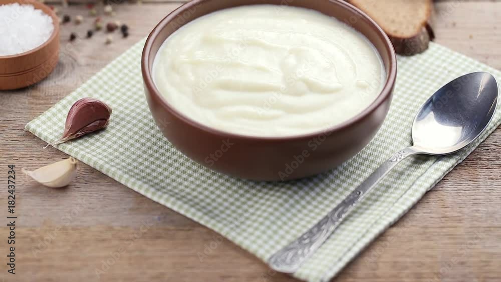 white cream soup in a ceramic plate on the table. under a plate a napkin in a green box. next to it there is salt, pepper is scattered, bread and garlic lie on the table white cream soup in a ceramic plate on the table. under a plate a napkin in a green box. next to it there is salt, pepper is scattered, bread and garlic lie on the table