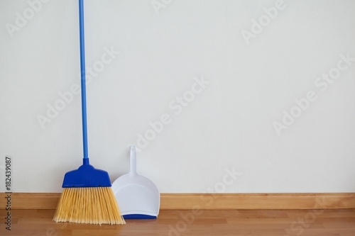 Dustpan and sweeping broom leaning against white wall photo