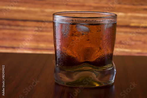 Glass of wiskey and ice on wooden background
