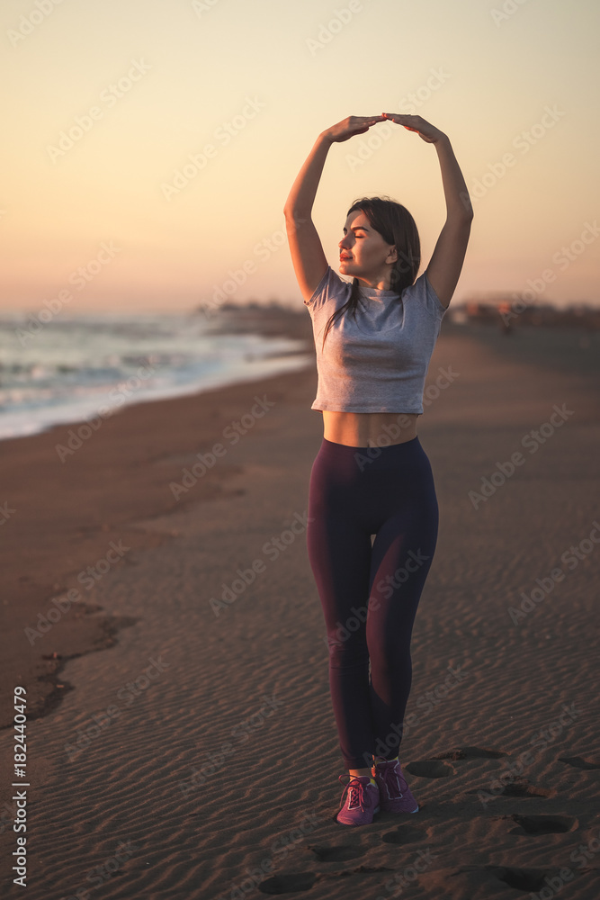 Beautiful young woman doing exercise on the sandy beach, healthy relaxation.