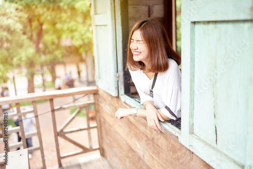 Beautiful asian girl smiling and relaxing at behide of wooden window after opening it.