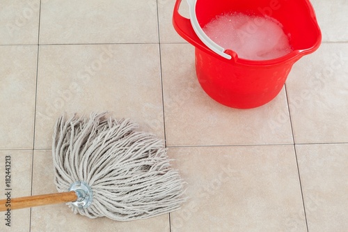 Bucket with foamy water and mopping the tile floor