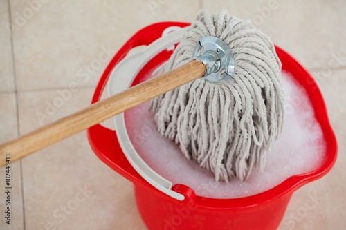 Bucket with foamy water and mopping the tile floor