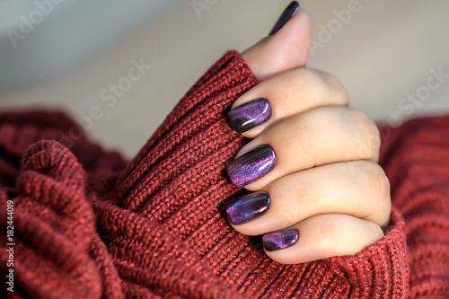 Beautiful nail polish in hand, purple nail art manicure, red background