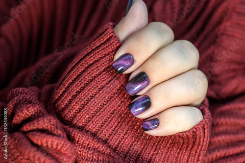 Beautiful nail polish in hand, purple nail art manicure, red background