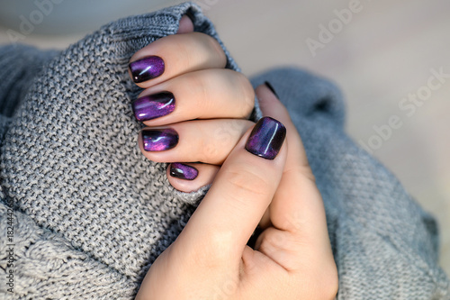 Beautiful nail polish in hand, purple nail art manicure, gray background