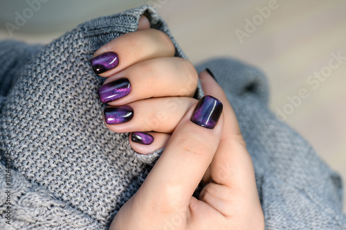 Beautiful nail polish in hand, purple nail art manicure, gray background
