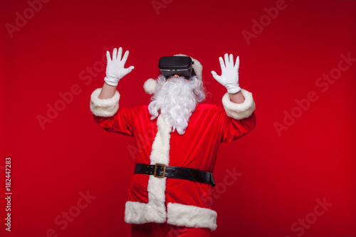 Santa Claus wearing virtual reality goggles, on a red background. Christmas