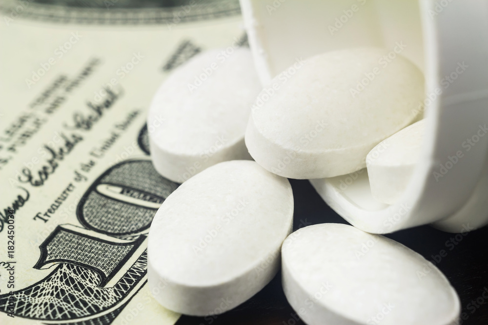 White pills of calcium, vitamin supplement, medical tablets in bottle on dollar banknote, macro image White pills of calcium, vitamin supplement, medical tablets in bottle on dollar banknote, macro image