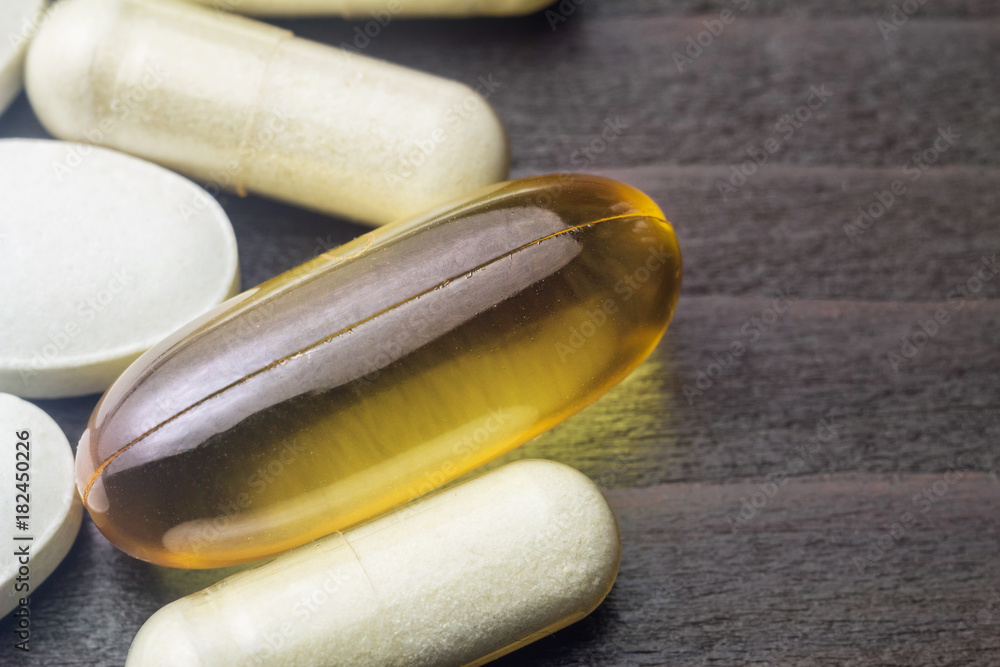 White capsules of glucosamine, yellow capsules of omega-3, white pills of calcium on wooden table, macro image White capsules of glucosamine, yellow capsules of omega-3, white pills of calcium on wooden table, macro image
