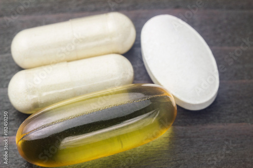 White capsules of glucosamine, yellow capsules of omega-3, white pills of calcium on wooden table, macro image photo