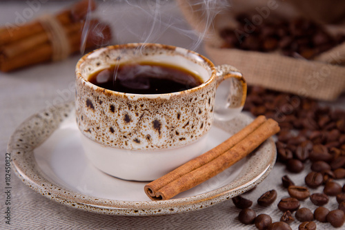Cup of black coffee and grains of coffee with cinnamon sticks.