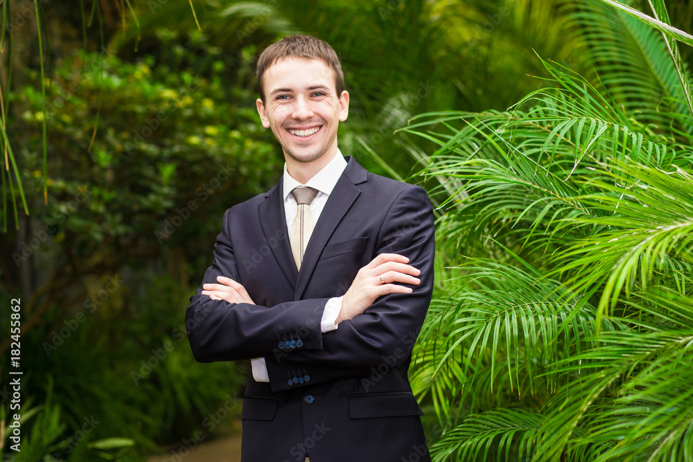 Happy smiling businessman in a business suit in the palm garden. Harmony with nature. Concept of a successful Happy smiling businessman in a business suit in the palm garden. Harmony with nature. Concept of a successful