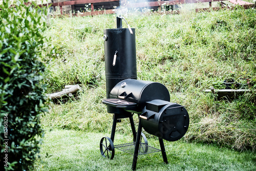 Black metal Locomotive grill with a pellet  smoker on green grass background 