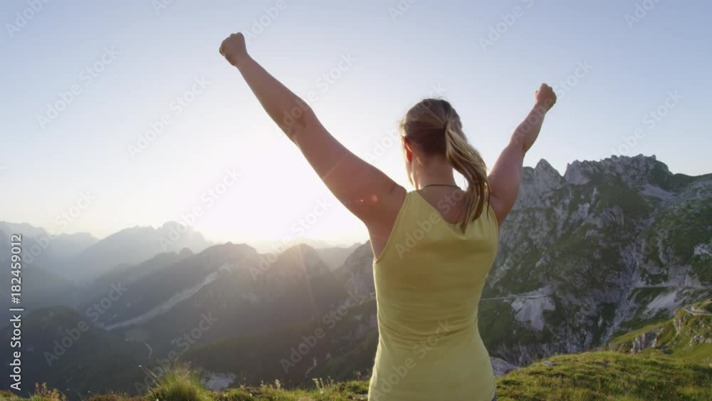 SLOW MOTION Happy woman raising her arms victoriously on rocky mountaintop at golden sunset. Hiking girl outstretching arms when reaching top of mountain at sunrise. Young trekker achieving daily goal SLOW MOTION Happy woman raising her arms victoriously on rocky mountaintop at golden sunset. Hiking girl outstretching arms when reaching top of mountain at sunrise. Young trekker achieving daily goal