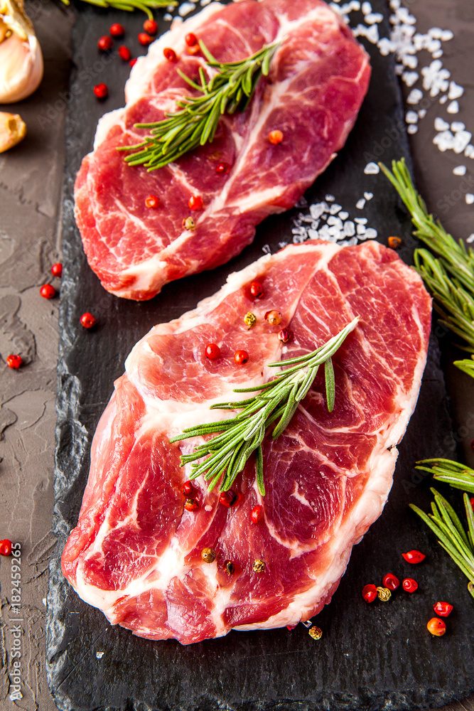 Close up of raw fresh meat. Steaks with herbs and spices on dark rustic background.