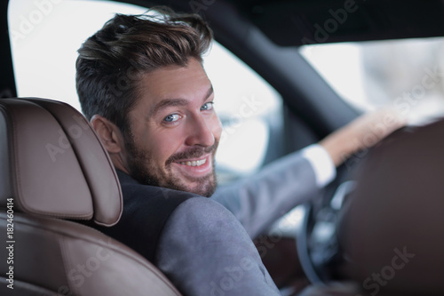 rear view, young man driving his car, looking at camera