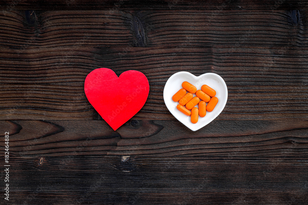 Treat heart. Pills in bowl in shape of heart on dark wooden background top view copyspace Treat heart. Pills in bowl in shape of heart on dark wooden background top view copyspace