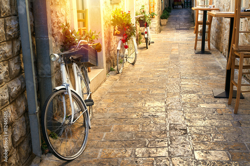 Stunning view of stoned paved street in old town on sunrise. Pots with flowers standing on vintage bicycles along a wall. Sun light on stone walls. Travel Montenegro