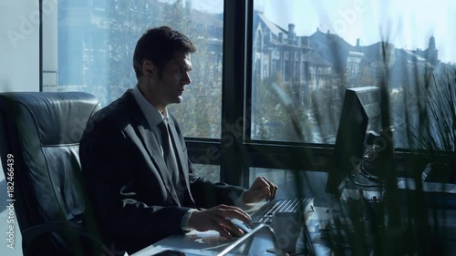 Slow motion footage of successful businessman sitting at a table and working at computer in modern office / Businessman working at office