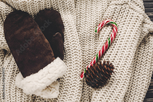 stylish gloves and knitted sweater with peppermint candy cane and cones on rustic background. winter atmospheric image, christmas flat lay, seasonal greetings