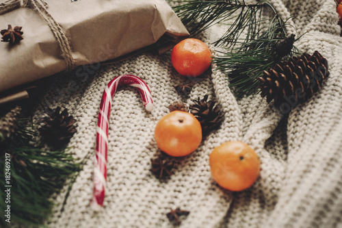 stylish craft gift and peppermint candy cane in heart and pine cones fir branches anise with tangerine on rustic knitted sweater top view, space for text.  seasonal greetings.  merry christmas concept photo