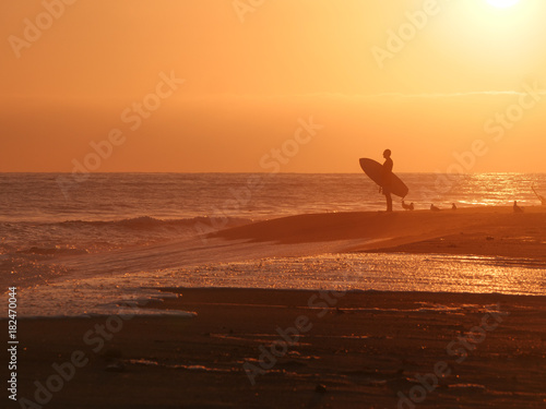 Surfer watching sunset on the beach holding surfboard