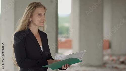 Female architect studying drafts while visiting large construction site photo