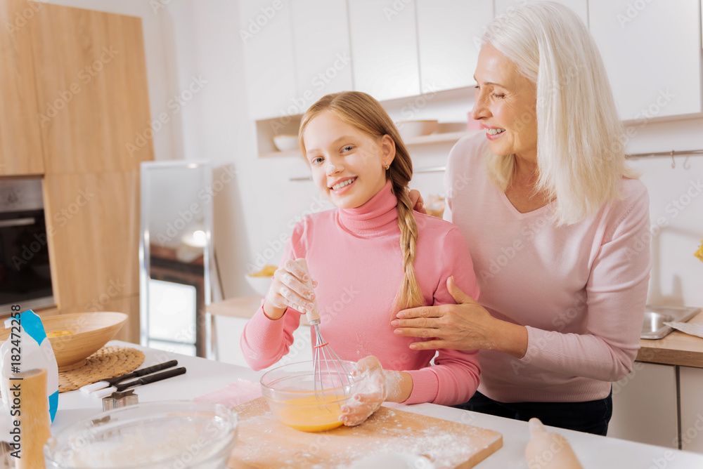 New skills. Positive nice joyful girl holding a whisk and whipping while learning how to cook New skills. Positive nice joyful girl holding a whisk and whipping while learning how to cook