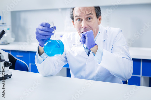 Something went wrong. Nice scared professional scientist holding a flask and biting his hand while feeling worried