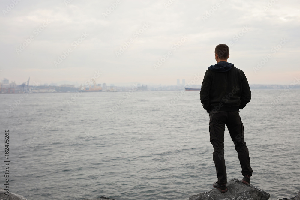 Man standing near the sea and looking at horizon, cloudy windy day. Thinking, Concentration, Loneliness concept. Man standing near the sea and looking at horizon, cloudy windy day. Thinking, Concentration, Loneliness concept.